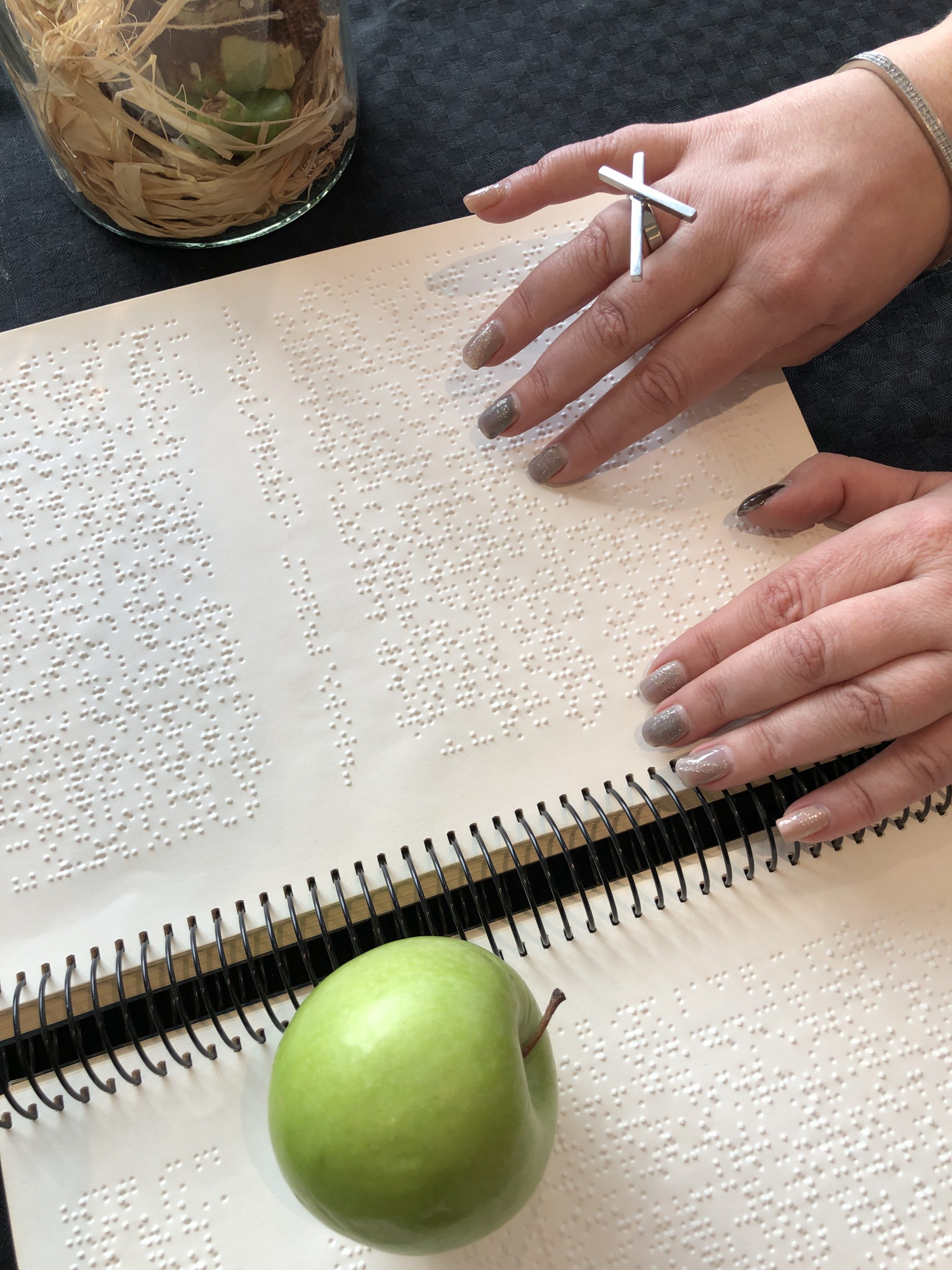 Bild - Händer som läser punktskrift med ett äpple bredvid